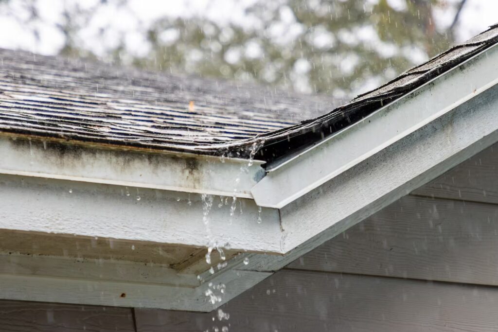 Rainwater overflowing from a damaged roof and clogged gutters, highlighting the need for timely gutter installation and repair.