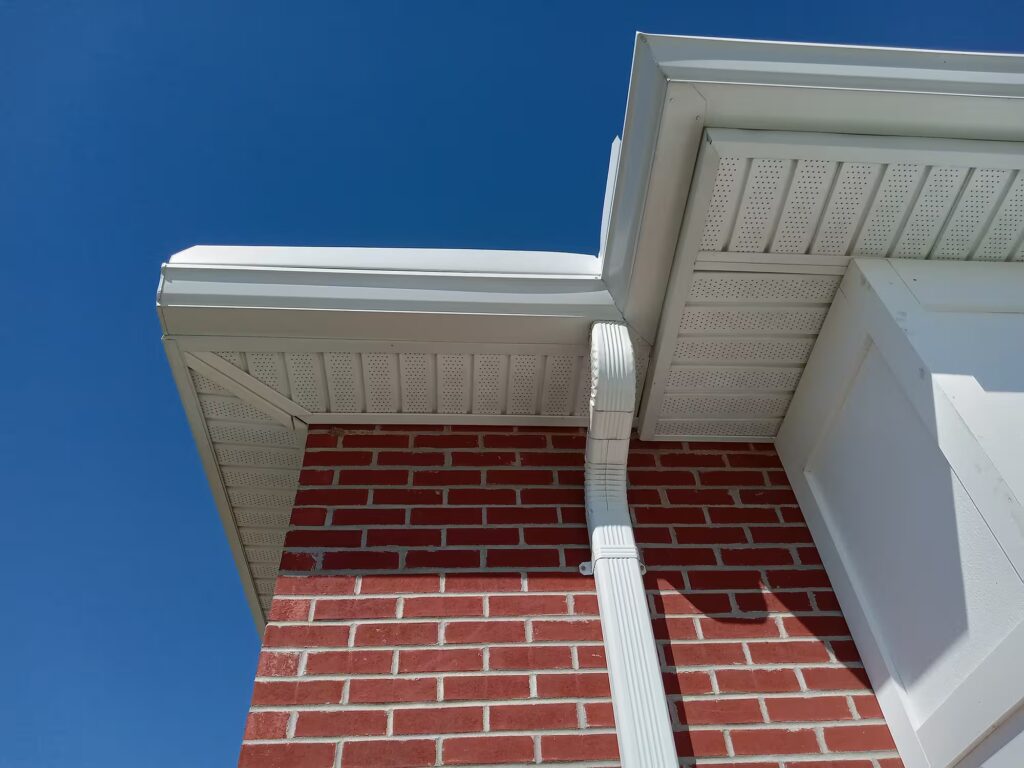 Close-up of newly installed seamless aluminum gutters and downspout on a brick home under a clear blue sky, showcasing professional gutter installation.