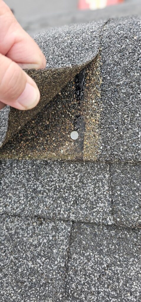 Close-up of worn asphalt shingles lifted during a roof inspection in McFarland, WI