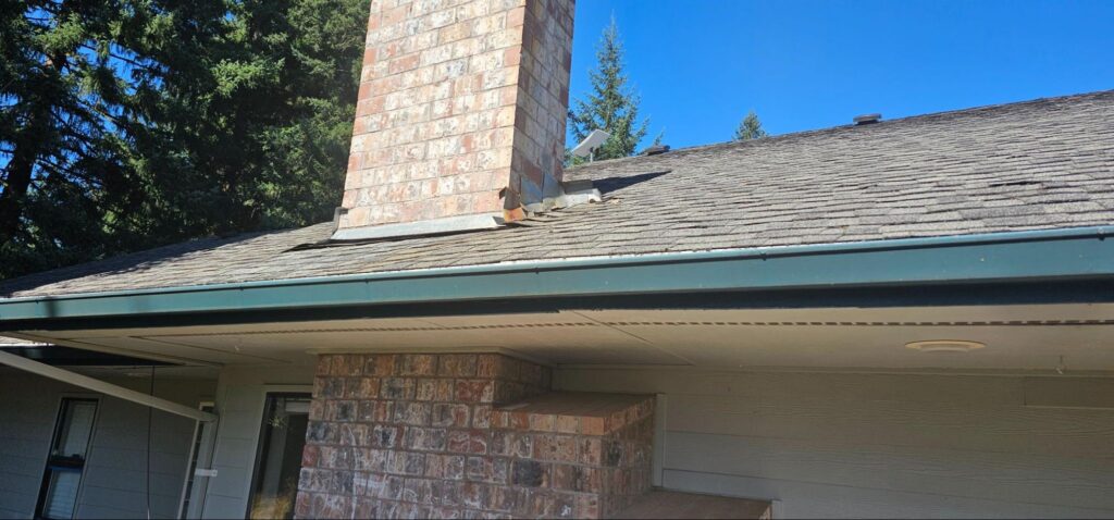 Close-up of asphalt shingle roof and brick chimney flashing during a Wisconsin roof inspection
